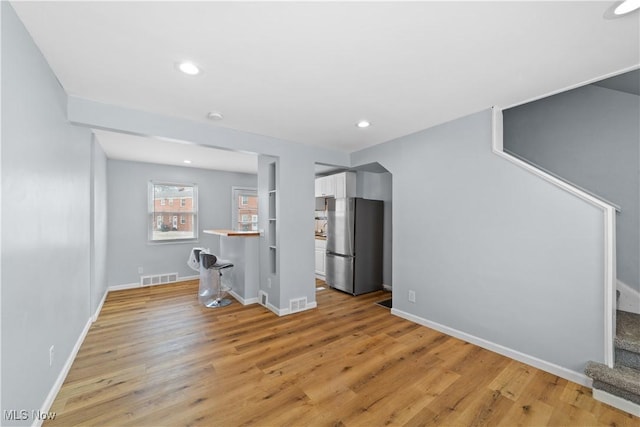 unfurnished living room with visible vents, baseboards, stairway, recessed lighting, and light wood-style flooring