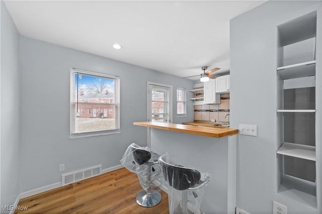 kitchen featuring visible vents, backsplash, wood finished floors, white cabinets, and wooden counters