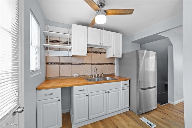 kitchen featuring butcher block countertops, white cabinets, freestanding refrigerator, and a sink