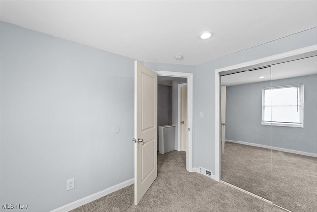 unfurnished bedroom featuring a closet, visible vents, light colored carpet, and baseboards