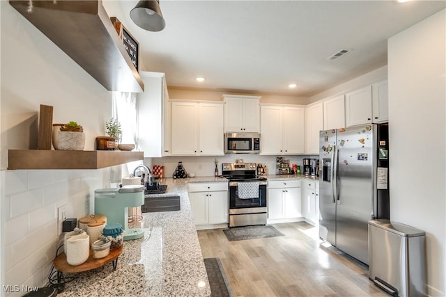 kitchen with a sink, light stone counters, white cabinetry, stainless steel appliances, and light wood-style floors