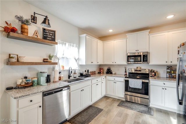 kitchen with light wood finished floors, tasteful backsplash, appliances with stainless steel finishes, white cabinets, and a sink