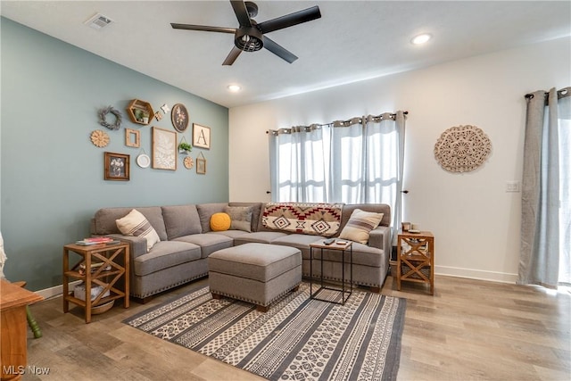 living room with ceiling fan, baseboards, visible vents, and light wood-type flooring