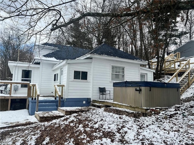 snow covered house with a deck, a shingled roof, and a hot tub