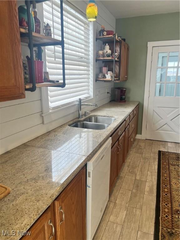 kitchen with brown cabinetry, light wood finished floors, open shelves, white dishwasher, and a sink