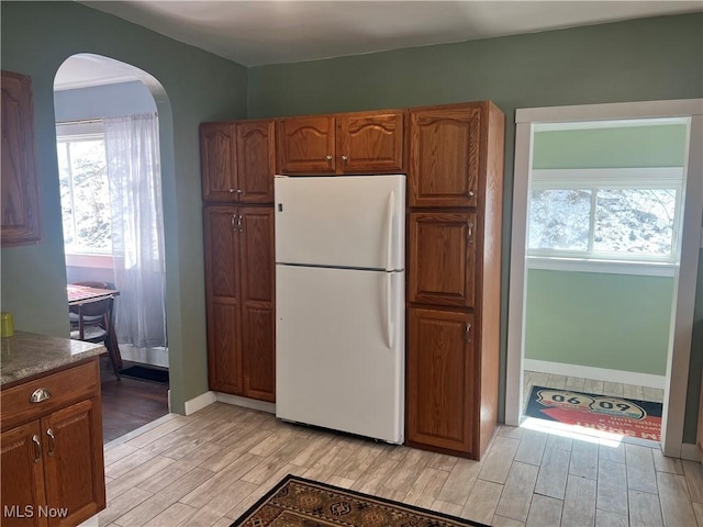 kitchen featuring a wealth of natural light, arched walkways, freestanding refrigerator, and wood finish floors