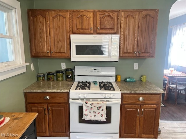 kitchen with white appliances, brown cabinetry, light wood-style floors, and arched walkways