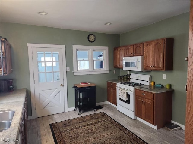 kitchen with baseboards, white appliances, brown cabinetry, and light wood finished floors