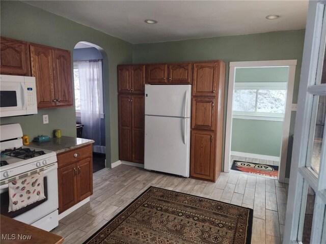 kitchen featuring arched walkways, white appliances, light wood-style floors, and plenty of natural light