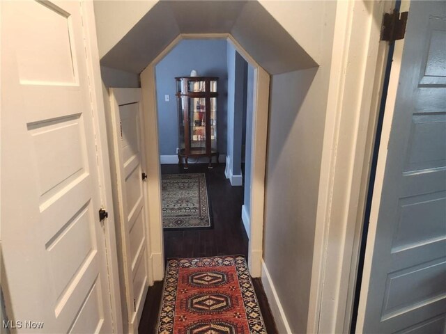 hallway with baseboards, dark wood finished floors, and vaulted ceiling