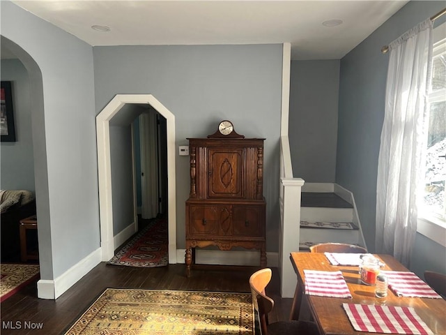 dining space featuring stairs, baseboards, arched walkways, and dark wood-style flooring