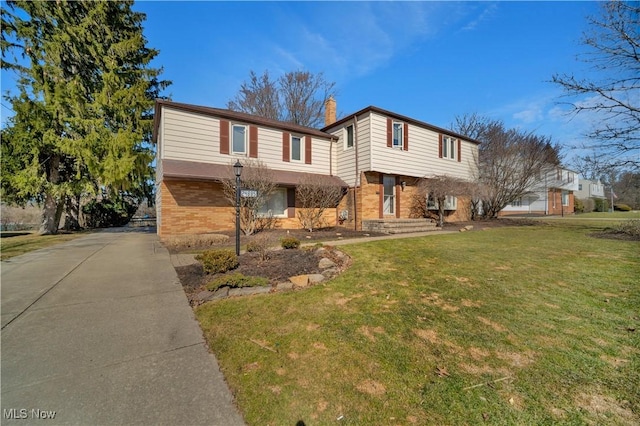 view of front of house with a front lawn, brick siding, driveway, and a chimney