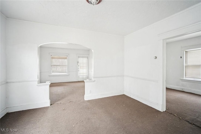 unfurnished room featuring arched walkways, plenty of natural light, and baseboards