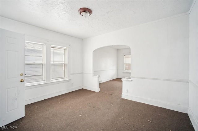 empty room featuring arched walkways, a healthy amount of sunlight, a textured ceiling, and baseboards