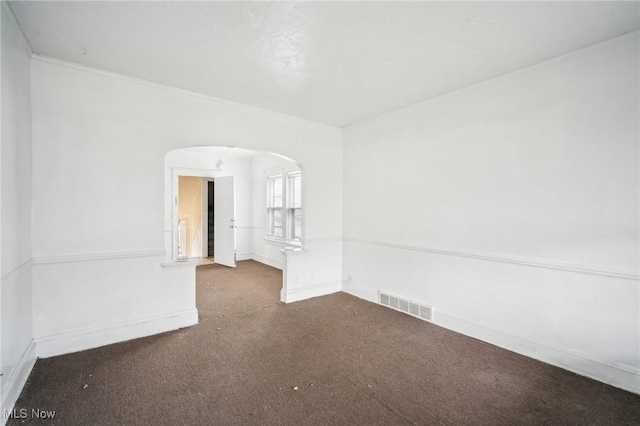 carpeted spare room with visible vents, arched walkways, and baseboards