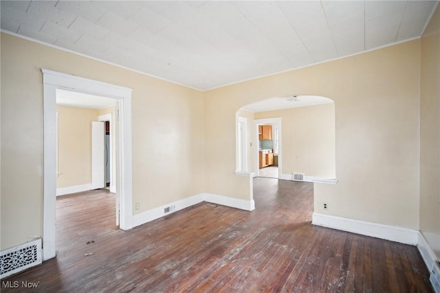 empty room featuring arched walkways, visible vents, baseboards, and wood-type flooring