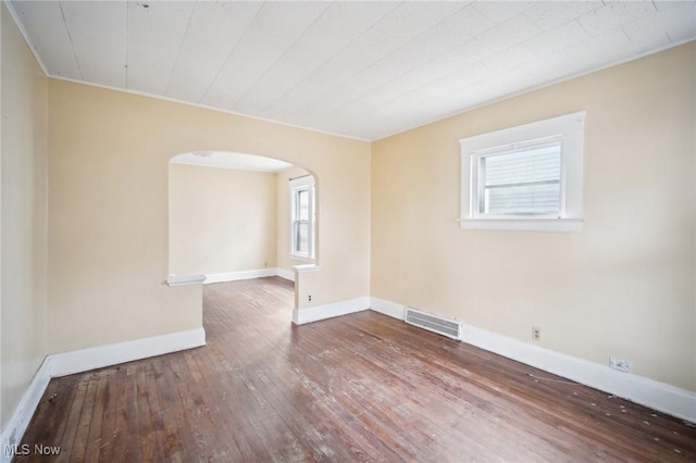 unfurnished room with visible vents, arched walkways, baseboards, and hardwood / wood-style floors