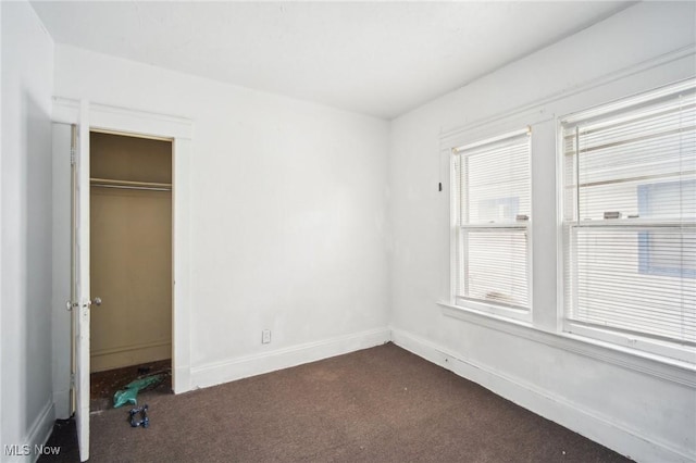 unfurnished bedroom featuring dark colored carpet, a closet, and baseboards