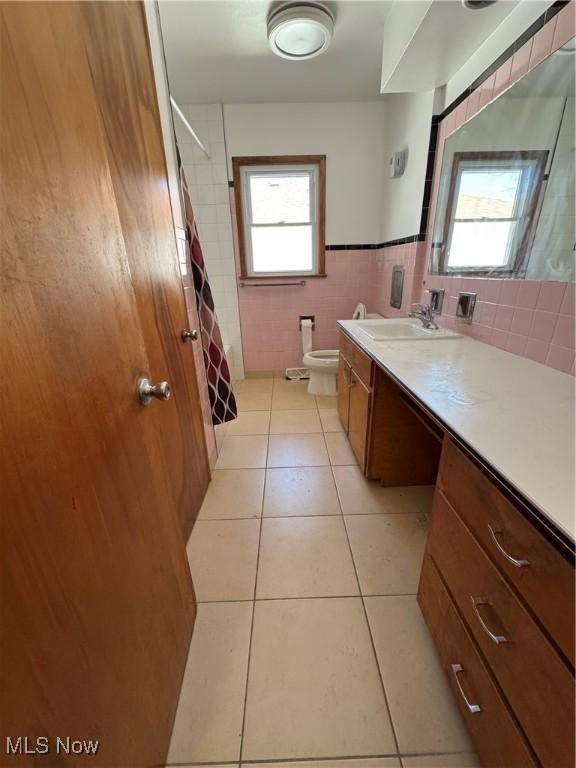 full bathroom featuring tile patterned flooring, curtained shower, tile walls, toilet, and vanity