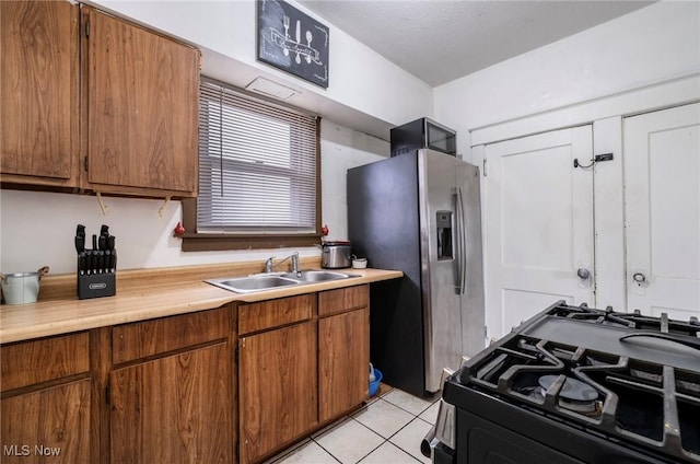 kitchen featuring black gas range oven, light tile patterned flooring, a sink, light countertops, and stainless steel fridge