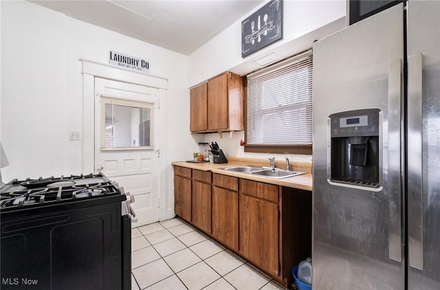 kitchen featuring a sink, black gas stove, stainless steel fridge, brown cabinetry, and light countertops