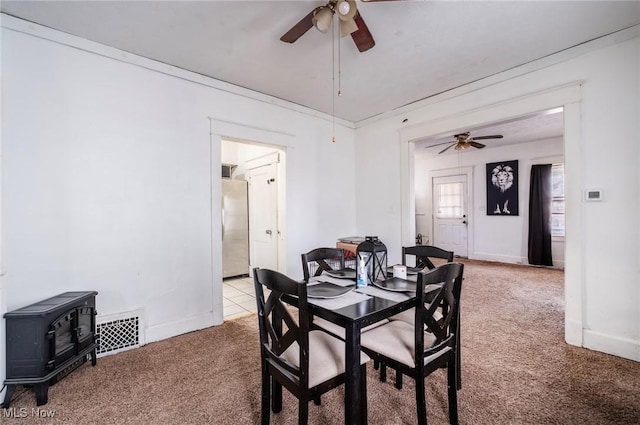 dining room featuring visible vents, light carpet, ceiling fan, and a wood stove