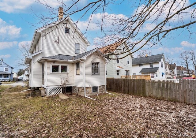 back of property with a residential view, roof with shingles, a chimney, and fence