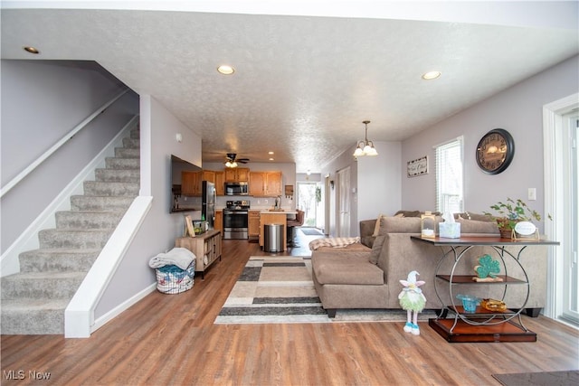 living area featuring light wood-style flooring, a textured ceiling, recessed lighting, stairway, and baseboards