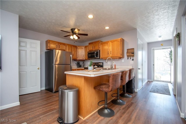 kitchen featuring a sink, dark wood finished floors, appliances with stainless steel finishes, a peninsula, and light countertops