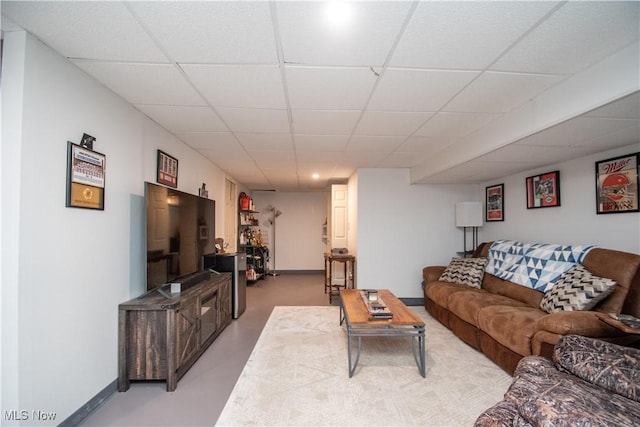 living room with a drop ceiling, baseboards, and concrete flooring