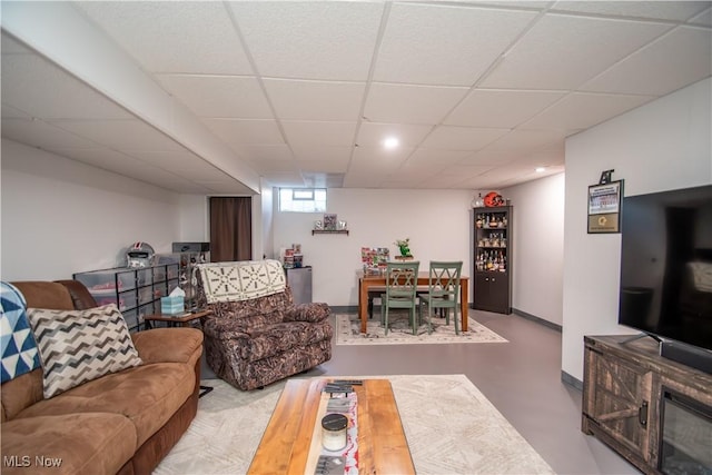 living room featuring finished concrete flooring, a paneled ceiling, and baseboards