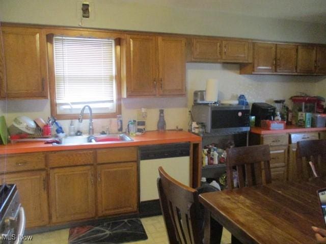 kitchen with brown cabinetry, a sink, stove, dishwasher, and stainless steel microwave