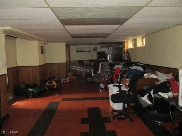 basement featuring a wainscoted wall, wood walls, and a paneled ceiling