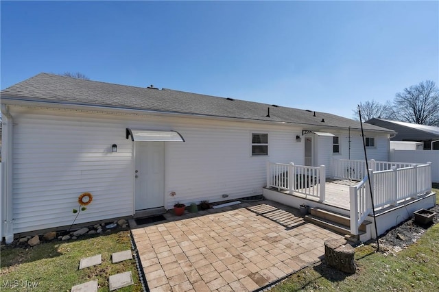 rear view of property featuring a wooden deck, a shingled roof, and a patio area