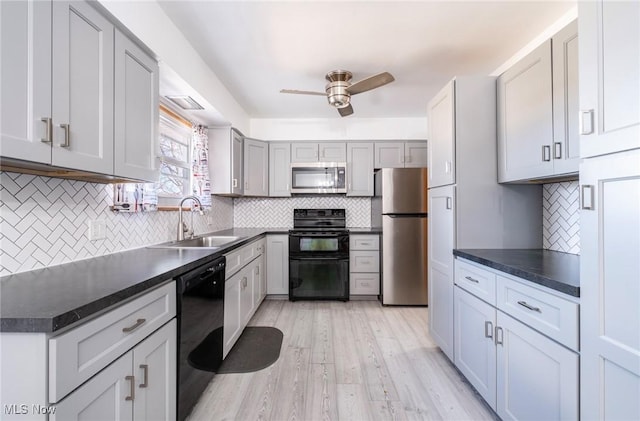 kitchen with dark countertops, light wood-style flooring, black appliances, a ceiling fan, and a sink