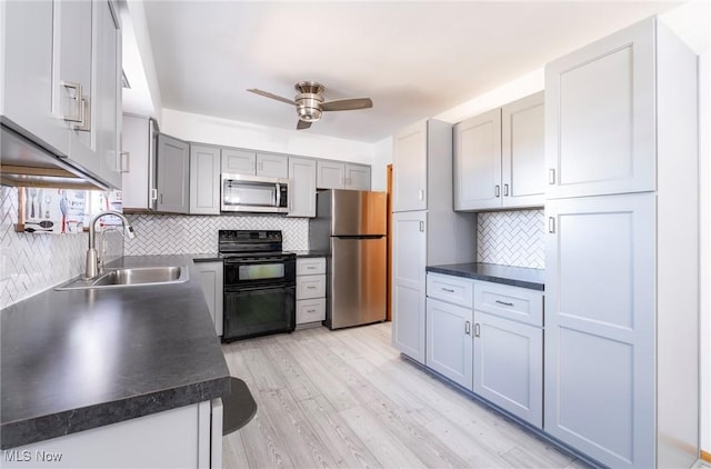 kitchen with dark countertops, light wood finished floors, stainless steel appliances, a ceiling fan, and a sink