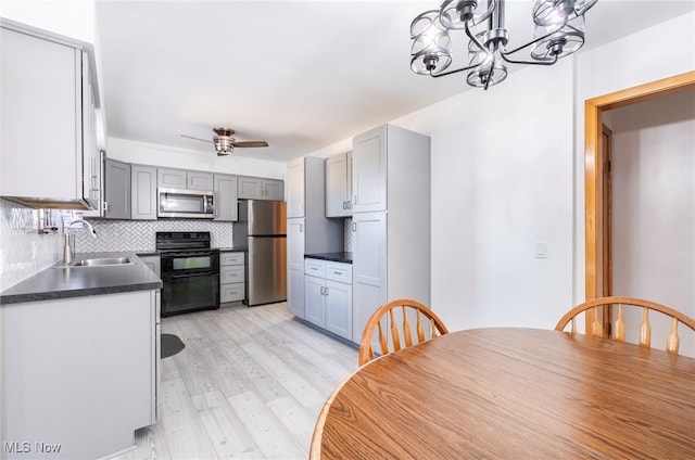 kitchen with light wood-style flooring, a sink, dark countertops, appliances with stainless steel finishes, and decorative backsplash