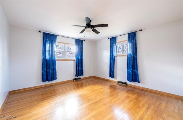 spare room featuring a ceiling fan, wood finished floors, visible vents, and a wealth of natural light