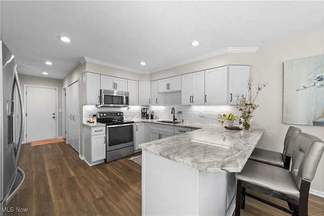 kitchen featuring a breakfast bar area, a peninsula, dark wood-style flooring, a sink, and stainless steel appliances