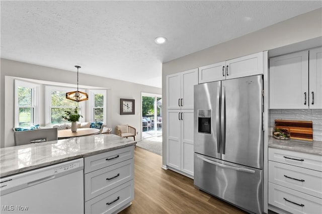 kitchen with light stone counters, stainless steel fridge, dishwasher, and white cabinets