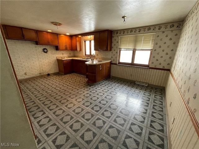 kitchen with light floors, wallpapered walls, a sink, light countertops, and brown cabinets