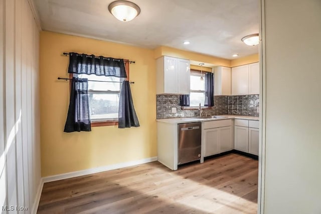 kitchen with a sink, backsplash, stainless steel dishwasher, white cabinetry, and light countertops