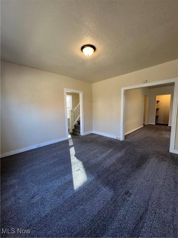 spare room featuring stairs, carpet flooring, baseboards, and a textured ceiling