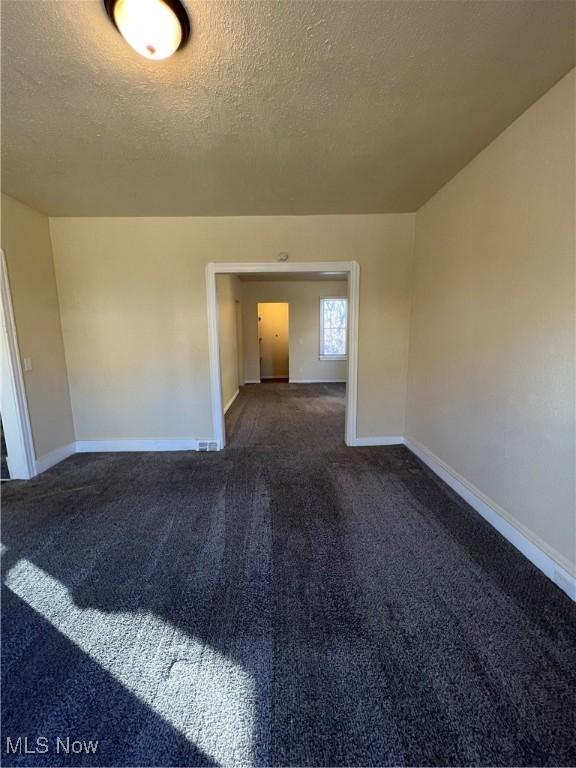 empty room with baseboards, a textured ceiling, and dark carpet