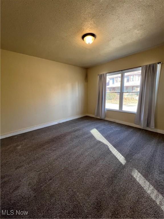 unfurnished room featuring baseboards, dark colored carpet, and a textured ceiling