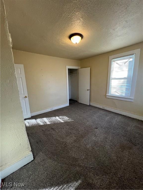 unfurnished bedroom featuring baseboards, carpet floors, a textured ceiling, and a closet