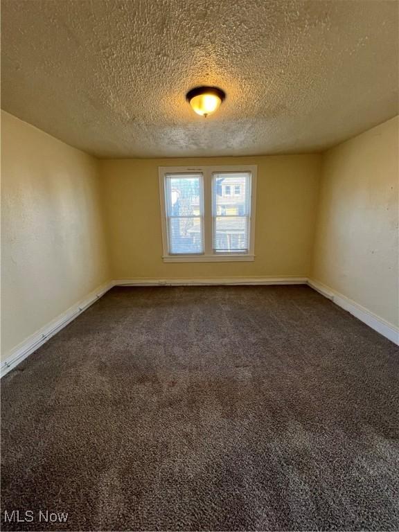 spare room with baseboards, dark colored carpet, and a textured ceiling