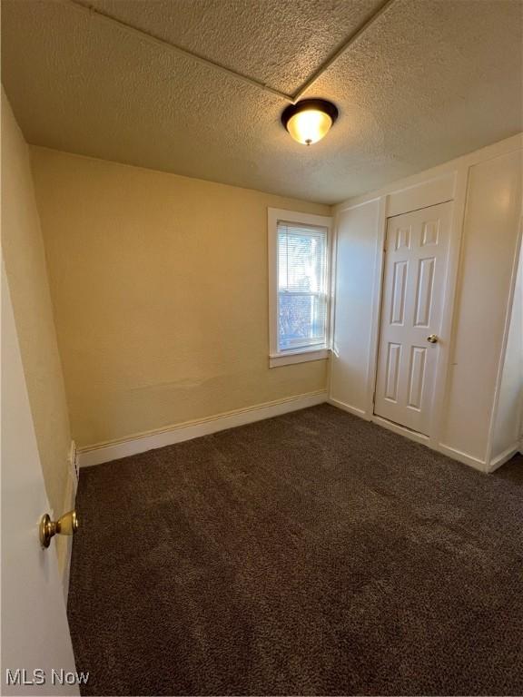 unfurnished bedroom featuring dark carpet, a textured ceiling, and baseboards