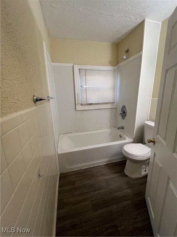 full bathroom featuring toilet, wood finished floors, a textured wall, and a textured ceiling