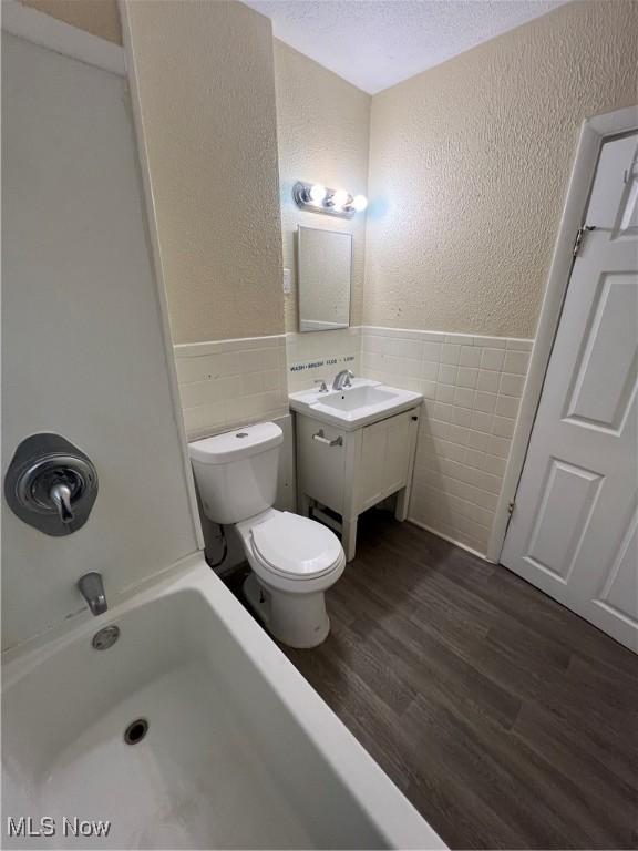 full bath with tile walls, a wainscoted wall, a textured wall, wood finished floors, and a textured ceiling